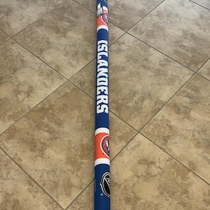 May include: A long, cylindrical item in blue, orange, and white, featuring the word "ISLANDERS" printed vertically. It displays the NHL logo and team graphics. This appears to be a sports-related accessory.