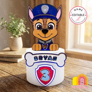 Può includere: Un cake topper cilindrico bianco con un personaggio di cane poliziotto dei cartoni animati con cappello e uniforme blu. Il topper ha una targhetta a forma di osso con la scritta "BRYAN" e uno scudo con il numero "3".