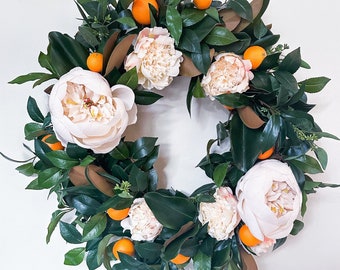 Può includere: Una ghirlanda verde con fiori bianchi e frutti arancioni. La ghirlanda è fatta di verde fresco e ha una varietà di fiori e frutti.