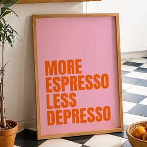 Könnte beinhalten: Ein gerahmter rosa Kunstdruck mit den Worten "MORE ESPRESSO LESS DEPRESSO" in orangefarbenen Blockbuchstaben. Der Druck befindet sich in einem hellen Holzrahmen. Eine Topfpflanze und ein Korb mit Orangen sind ebenfalls im Bild.