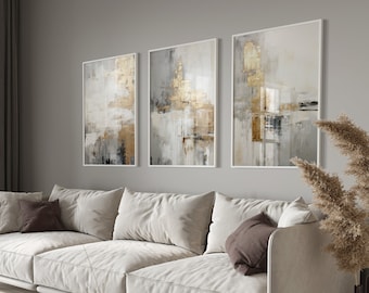 May include: A white sectional sofa with brown throw pillows in a living room with three abstract paintings with gold and gray tones on the wall. The paintings are in white frames. There is a vase with a single stem on a wooden coffee table in front of the sofa.