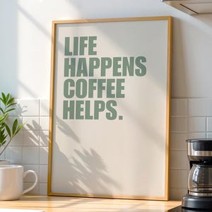 May include: A framed print with the text "LIFE HAPPENS COFFEE HELPS." in green lettering on a cream background.