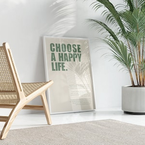 Pu&ograve; includere: Una stampa incorniciata con il testo "CHOOSE A HAPPY LIFE." in testo verde su uno sfondo beige. La stampa &egrave; appoggiata a un muro bianco accanto a una sedia in vimini e una pianta in vaso.