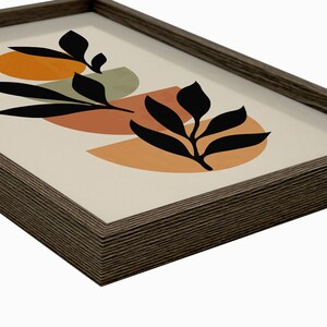 Puede incluir: Una impresi&oacute;n enmarcada con un dise&ntilde;o minimalista que presenta formas abstractas en tonos naranja, marr&oacute;n y verde. Las formas se superponen y se superponen, creando una sensaci&oacute;n de profundidad. Siluetas negras de hojas se colocan encima de las formas, agregando un toque de naturaleza al dise&ntilde;o.