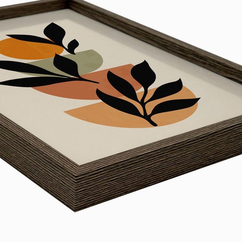 Puede incluir: Una impresi&oacute;n enmarcada con un dise&ntilde;o minimalista que presenta formas abstractas en tonos naranja, marr&oacute;n y verde. Las formas se superponen y se superponen, creando una sensaci&oacute;n de profundidad. Siluetas negras de hojas se colocan encima de las formas, agregando un toque de naturaleza al dise&ntilde;o.