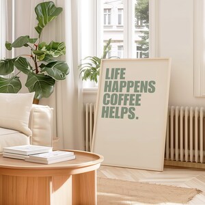 May include: A framed print with the text "Life Happens Coffee Helps." in green lettering on a white background. The print is hanging on a white wall in a living room setting.