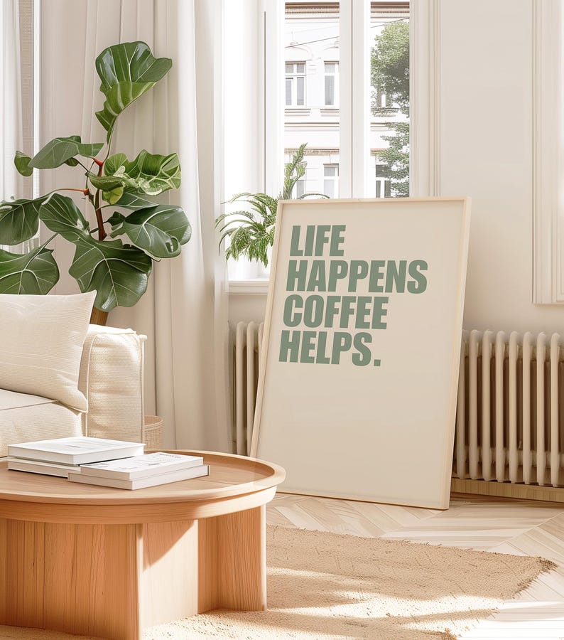May include: A framed print with the text "Life Happens Coffee Helps." in green lettering on a white background. The print is hanging on a white wall in a living room setting.