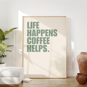 May include: A framed print with the text "LIFE HAPPENS COFFEE HELPS." in a sage green color on a cream background.