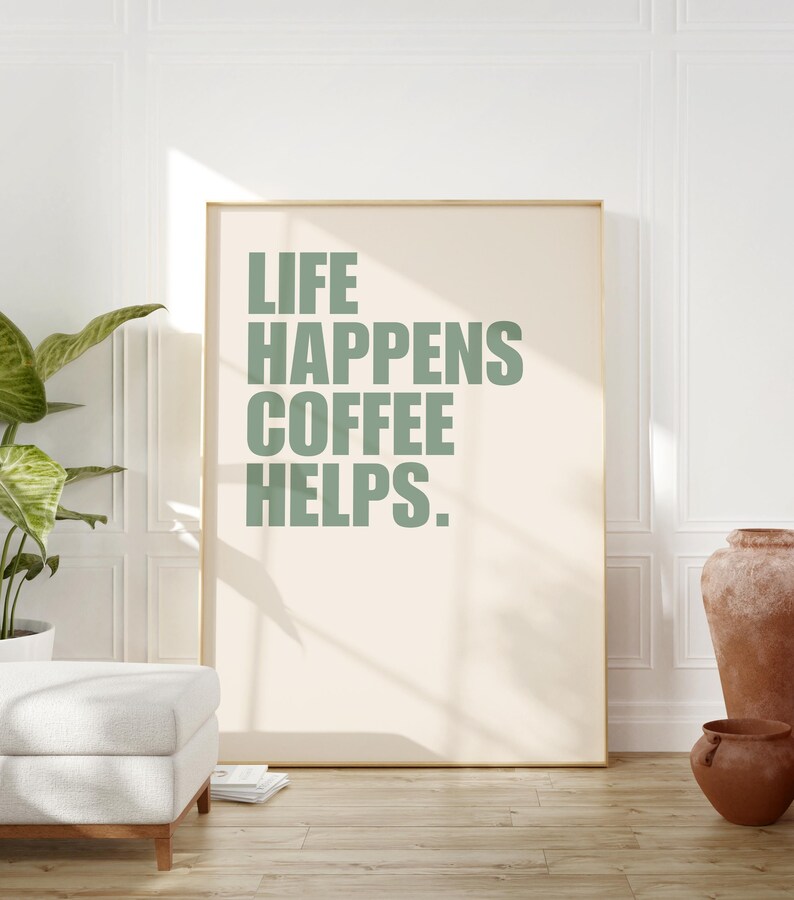 May include: A framed print with the text "LIFE HAPPENS COFFEE HELPS." in a sage green color on a cream background.