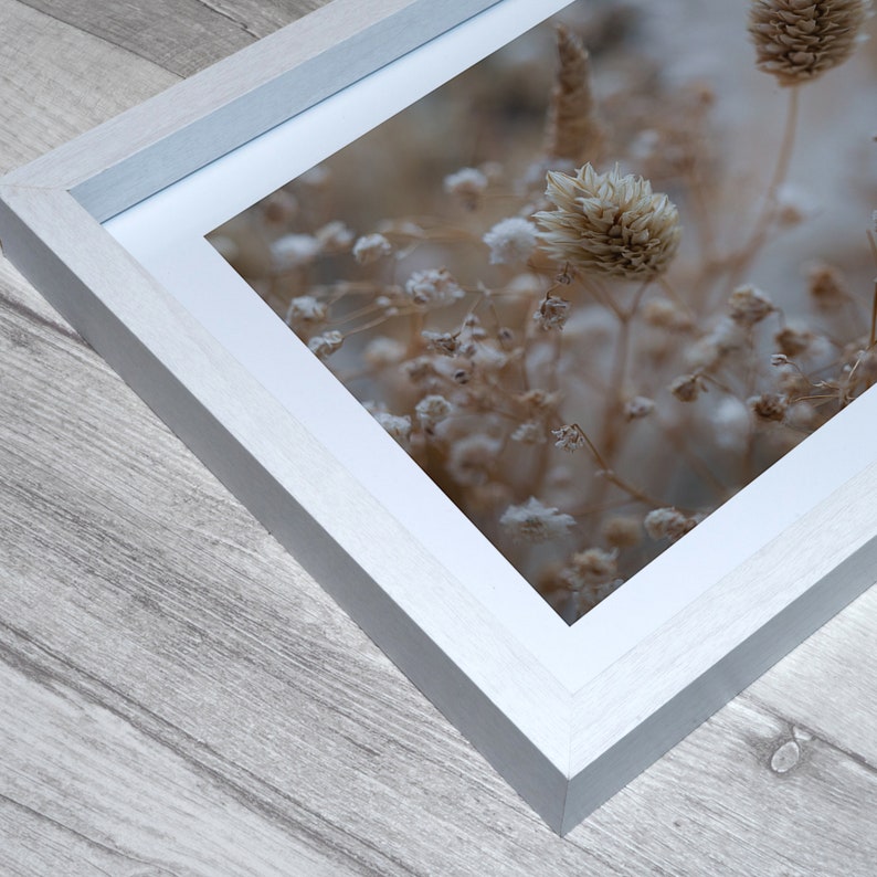 Puede incluir: Un marco de fotos blanco con un passe-partout, que muestra una fotograf&iacute;a de flores secas en tonos beige y marr&oacute;n. Las flores est&aacute;n dispuestas en un racimo, creando una composici&oacute;n suave y delicada.