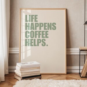 May include: A framed print with a light beige background and green text that reads "Life Happens Coffee Helps."