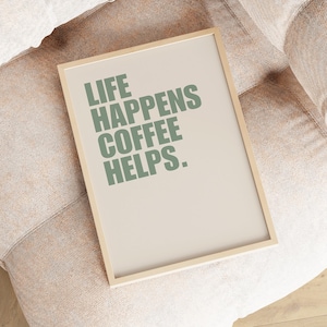 May include: A framed print with the text "Life Happens Coffee Helps." in green lettering on a beige background.