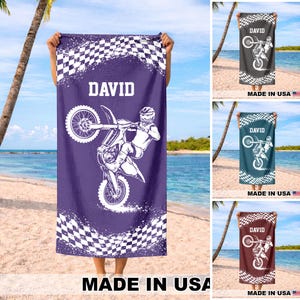 May include: A beach towel with a purple background featuring a white motocross rider performing a stunt. The towel has a checkered flag design and the name "DAVID" in white. The words "MADE IN USA" are at the bottom.