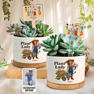 Puede incluir: Dos macetas de cerámica blanca con suculentas, cada una con un gráfico de "Plant Lady" y un letrero que dice "Retired Ashley 2025". Una maceta tiene una foto y un nombre personalizados. Las macetas están sobre bases de madera.