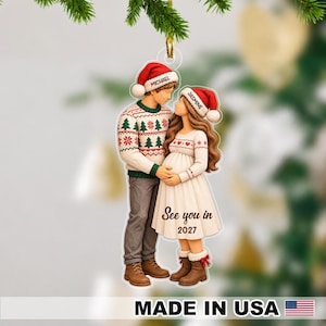 May include: A flat Christmas ornament featuring a couple wearing Santa hats with the names Michael and Jasmine printed on them. The couple wears festive sweaters and the dress has the text See you in 2027 printed on the front.