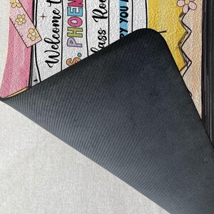 May include: Welcome to Ms. Phoenix's Class Room doormat with a pink, yellow and white design. The doormat has a black backing.