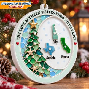 Op de afbeelding: Een ronde witte kerstornament met een 3D-reliëfdruk van een groene kerstboom en drie Amerikaanse staatskaarten gelabeld Lily, Sophia en Emma. De tekst luidt THE LOVE BETWEEN SISTERS KNOW NO DISTANCE met kleine rode hartjes aan de zijkanten.