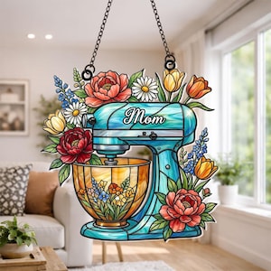 May include: A stained glass-style kitchen mixer with the word "Mom" in script. The mixer is teal with a gold bowl, surrounded by colorful flowers including red peonies, yellow tulips, and white daisies. It hangs from a black chain.