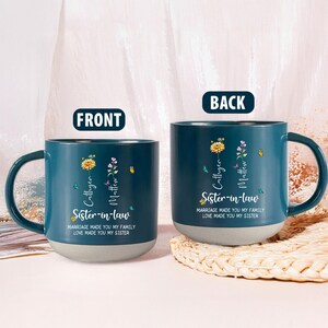 May include: Two teal ceramic mugs with a gray base. Each mug features floral designs, butterflies, and the text "Cathyen, Matthew, Sister-in-law, Marriage made you my family, Love made you my sister."