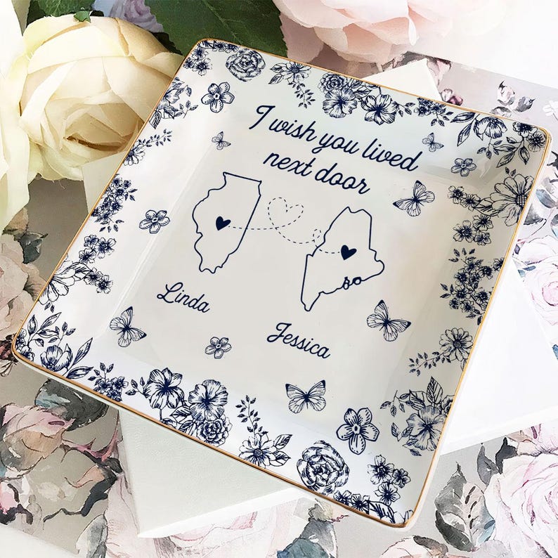 May include: Square white ceramic dish with a gold rim, featuring a floral and butterfly design in navy blue. The dish has the text "I wish you lived next door" with two state outlines and names.