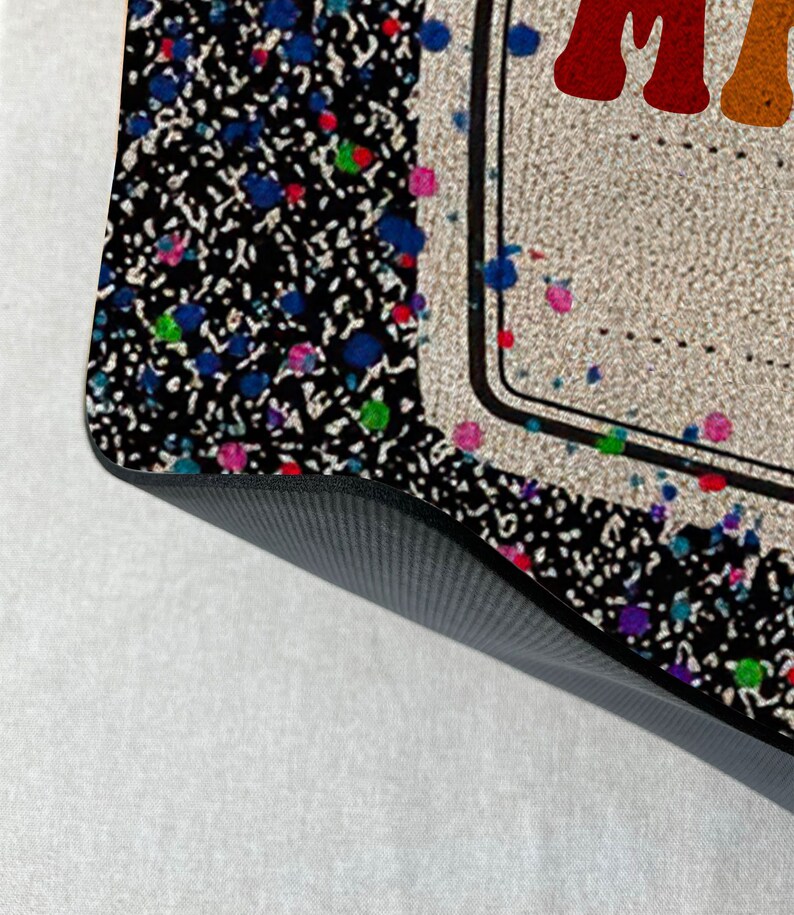 May include: A black and white patterned doormat with colorful paint splatters. The doormat has a black border and a white background with the word "Make" in rainbow letters.