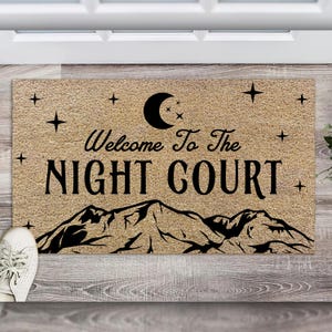 May include: Welcome to the Night Court doormat with a black crescent moon, stars, and mountain range design on a tan background.