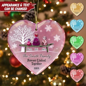 May include: A heart-shaped Christmas ornament with a pink hue. It depicts a family of three figures on a bench, with the names "Anna, Dad, Mom" below. The text "The Smith Family Forever Linked Together 2025" is also visible on the ornament.