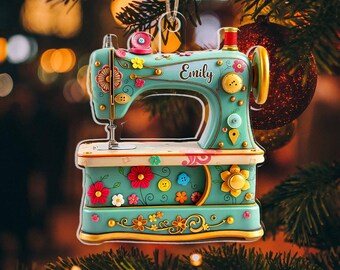 May include: A teal sewing machine Christmas ornament with floral and button accents. The ornament has gold trim and the name "Emily" is written on the side. The ornament is hanging from a string against a blurred background of Christmas lights and a tree.
