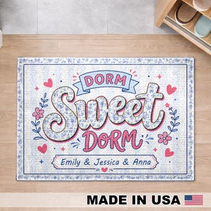 May include: A rectangular area rug featuring the text DORM SWEET DORM in blue and pink lettering. The design includes floral patterns, small red hearts, and the names Emily & Jessica & Anna printed in a central banner on a white background.