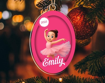 May include: A personalised Christmas tree decoration. The pink oval ornament features a cartoon ballerina in a pink tutu, the name "Emily" in white script, and the year "2025". The decoration hangs from a gold string on a Christmas tree.