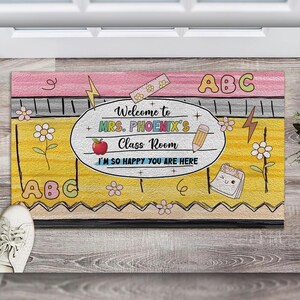 May include: A yellow and pink welcome mat with the text "Welcome to Mrs. Phoenix's Class Room I'm so happy you are here" and the letters "ABC" on either side.