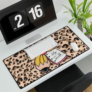 May include: A rectangular desk mat with a leopard print design. A large pencil and notepad graphic is centered on the mat. The notepad has the text "Ms. Smith". A white keyboard and mouse are on the mat.