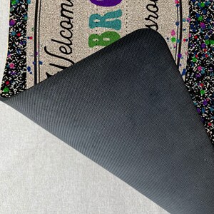May include: Welcome to the Brown Room doormat with a black and white confetti design. The doormat has a black non-slip backing.