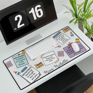 May include: A white desk mat with a grid pattern and colorful illustrations of school supplies. The text "Miss Michelle" is written in a pink script font. The text "REMINDER: to teach is to touch a life forever." is written in a black and white box. The text "TODAY'S GOAL: keep the tiny humans alive" is written in a black and white box. The text "REMINDER: the influence of a good teacher cannot be erased" is written in a black and white box. The text "BE PART of the world, the people and the difference you make" is written in a black and white box.