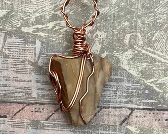 May include: A copper wire wrapped pendant featuring a brown and tan stone with a natural, irregular shape.