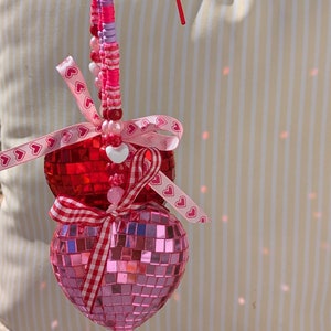 May include: Two pink and red heart-shaped ornaments with pink and white ribbon and beads.
