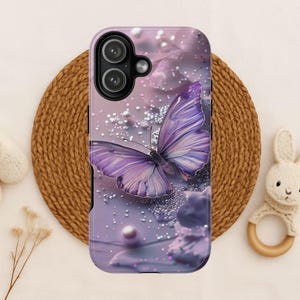 May include: A phone case featuring a purple butterfly design. The butterfly has detailed wing patterns and is set against a soft, lavender background with pearl accents. The case has a glossy finish and a camera cutout.