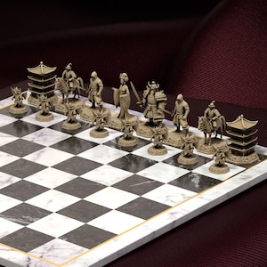 May include: A complete chess set featuring intricately detailed, tan-colored pieces representing Japanese samurai and historical figures. The chess board has a black and white checkered pattern with a gold border.