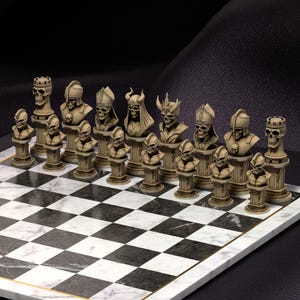 Puede incluir: Un juego de ajedrez completo con piezas temáticas de calaveras. Las piezas beige están detalladas, con varios diseños de calaveras que representan diferentes figuras de ajedrez. El tablero es de mármol con cuadros blancos y negros, y un borde dorado.