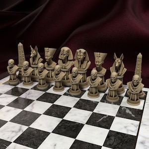 Könnte beinhalten: Ein komplettes Schachspiel mit Figuren, die antiken ägyptischen Figuren nachempfunden sind. Die beigefarbenen Figuren stehen auf einem schwarz-weiß karierten Marmorbrett. Der Hintergrund ist ein dunkelroter Stoff.