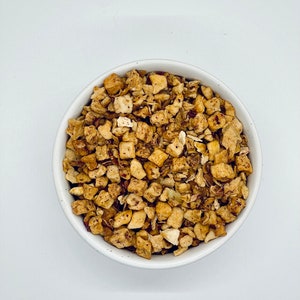 May include: A white bowl filled with dried apple pieces and cinnamon sticks. The apple pieces are a light brown color and the cinnamon sticks are a dark brown color.