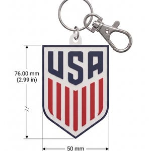 May include: A shield-shaped keyring featuring the text USA in navy blue above red vertical stripes on a white background. The keyring measures 76.00 mm in height and 50 mm in width, and includes a silver metal split ring and lobster clasp attachment.