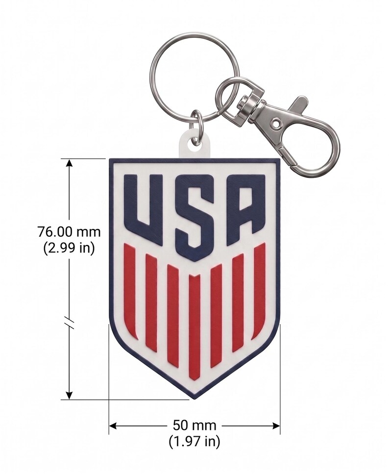 May include: A shield-shaped keyring featuring the text USA in navy blue above red vertical stripes on a white background. The keyring measures 76.00 mm in height and 50 mm in width, and includes a silver metal split ring and lobster clasp attachment.