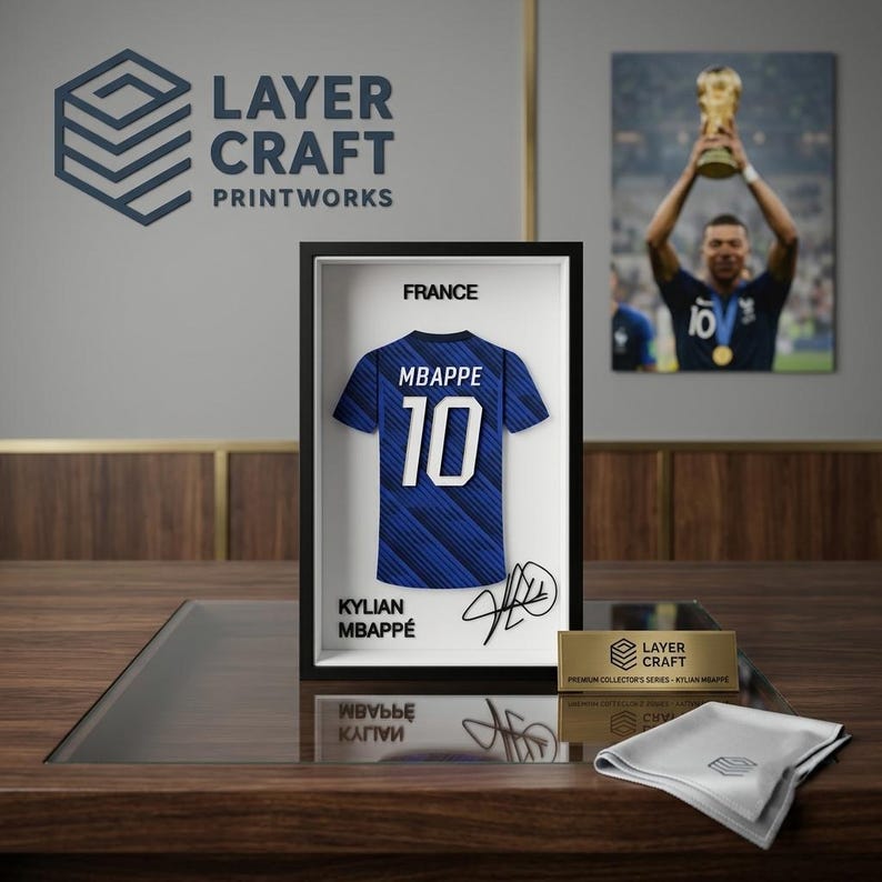 Peut inclure: Un cadre 3D pr&eacute;sentant un maillot de football bleu de la France avec le nom MBAPPE et le num&eacute;ro 10 en blanc. L'affichage inclut le texte FRANCE, KYLIAN MBAPPE et une signature. Une plaque dor&eacute;e indique LAYER CRAFT PREMIUM COLLECTOR'S SERIES.
