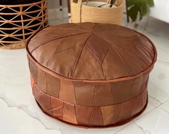 Può includere: Un pouf ottomano in pelle marrone con un motivo geometrico. Il pouf è realizzato con più pezzi di pelle cuciti insieme.