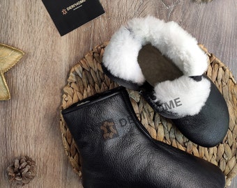 May include: Two pairs of black leather slippers with white fur lining. The slippers are on a woven straw mat. The brand name "DERIHOME" is visible on a black card.