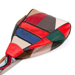 May include: A multi-colored leather backpack with a patchwork design. The bag has a red, white, blue, green, brown, and gray color scheme. The bag has a zipper closure and a strap.