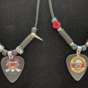 Puede incluir: Dos collares con colgantes de púas de guitarra. Uno presenta el logo de Metallica, el otro el logo de Guns N' Roses. Ambos tienen cordones negros, detalles metálicos y cuentas de calavera. El collar de Guns N' Roses tiene cuentas de rosas rojas.