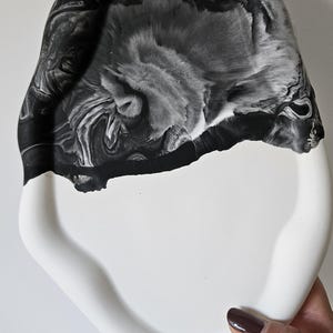 May include: A white ceramic tray with a black marbled design. The tray has a unique, organic shape and a smooth, glossy finish.
