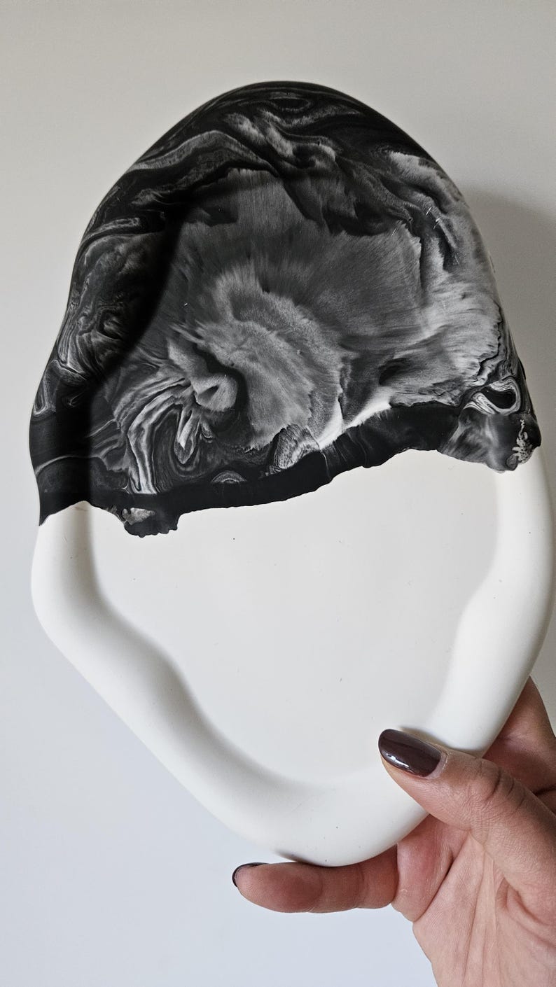May include: A white ceramic tray with a black marbled design. The tray has a unique, organic shape and a smooth, glossy finish.